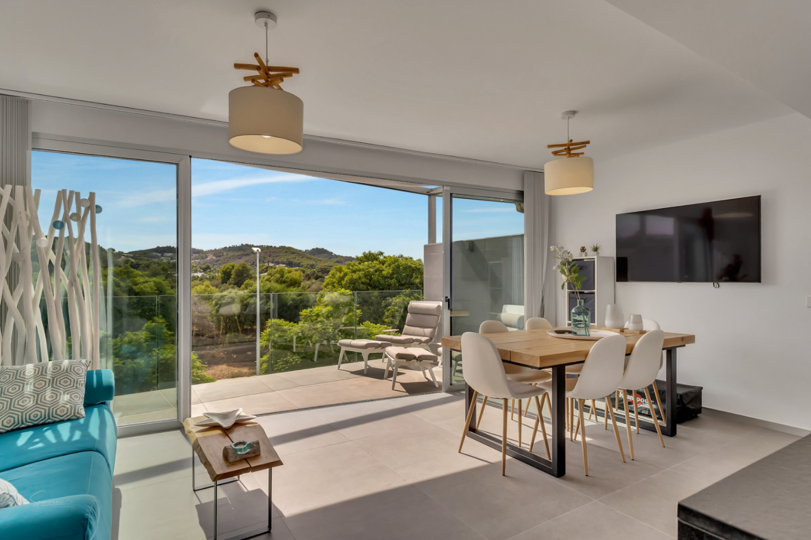 Heller, offener Wohn- und Essbereich mit großen Glasschiebetüren zum Balkon und Blick ins Grüne. Ausgestattet mit einem Holztisch, modernen Stühlen und Fliesenboden.