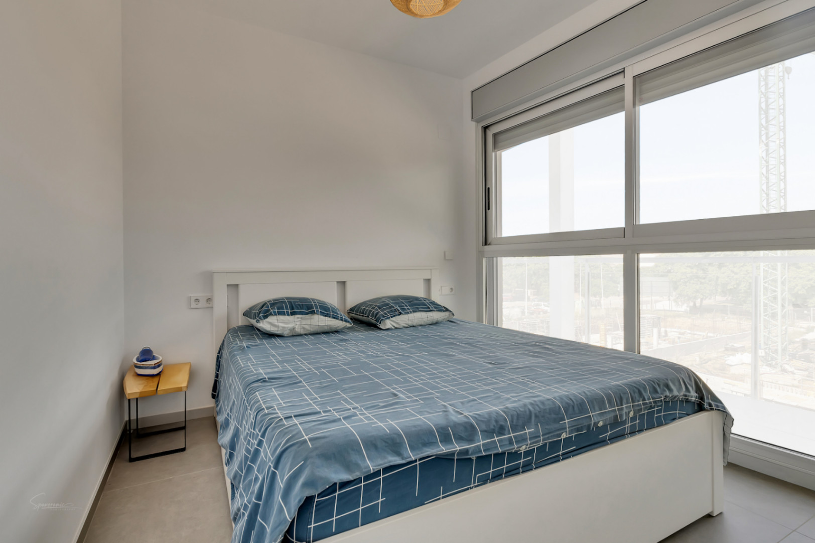 Helles Schlafzimmer mit Doppelbett, großen Schiebefenstern mit grauen Rahmen und integrierten elektrischen Jalousien für optimalen Komfort.