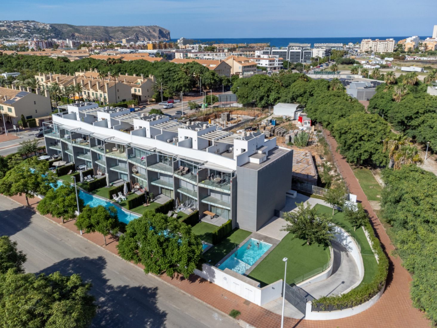 Luftaufnahme der modernen Wohnanlage mit zeitgenössischer Architektur, Gemeinschaftspools, angelegten Gärten und Panoramablick auf das Meer und die Berge.