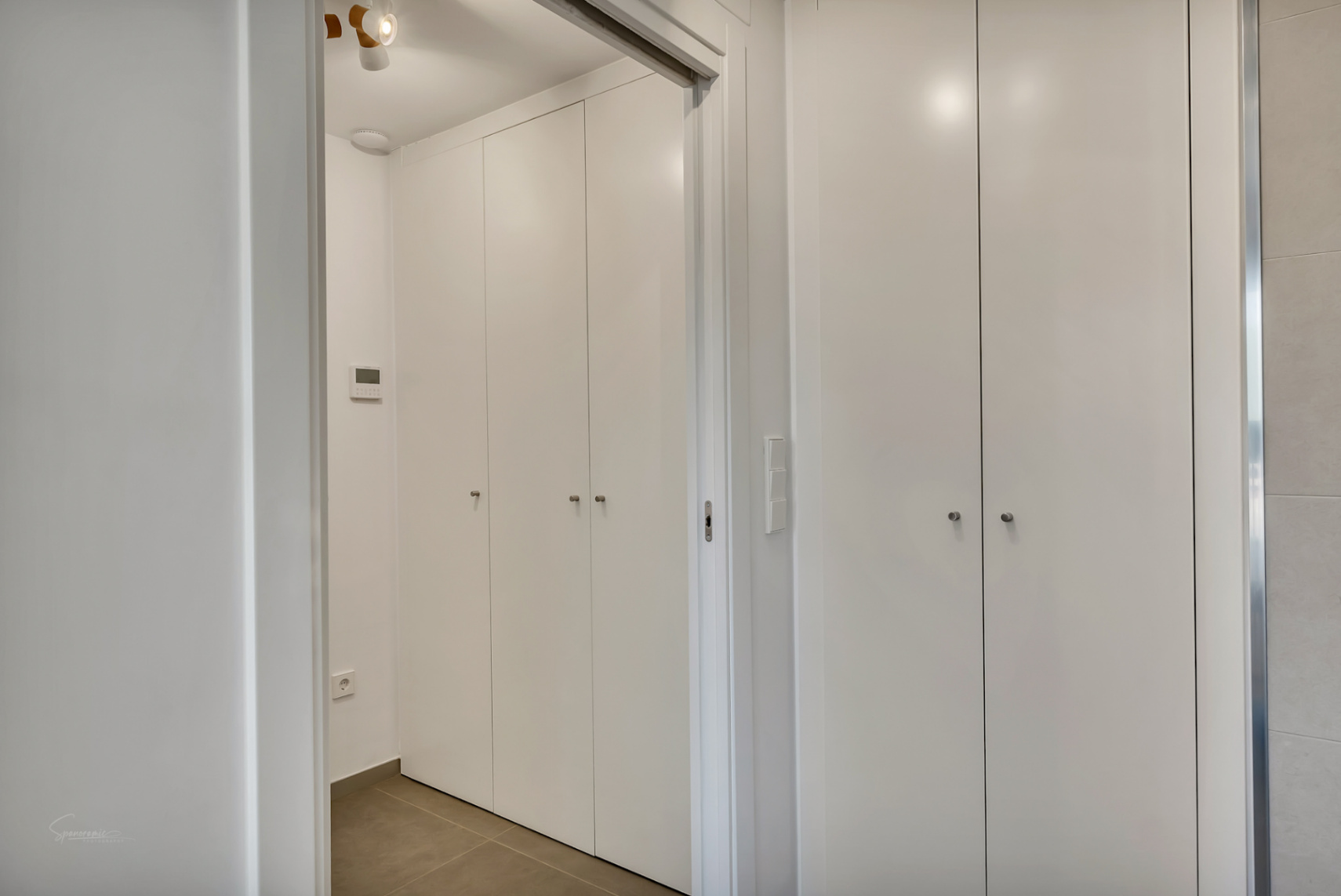 Moderner Flur mit raumhohen weißen Einbauschränken, minimalistischen Griffen und integrierter Steuerungseinheit an der Wand.