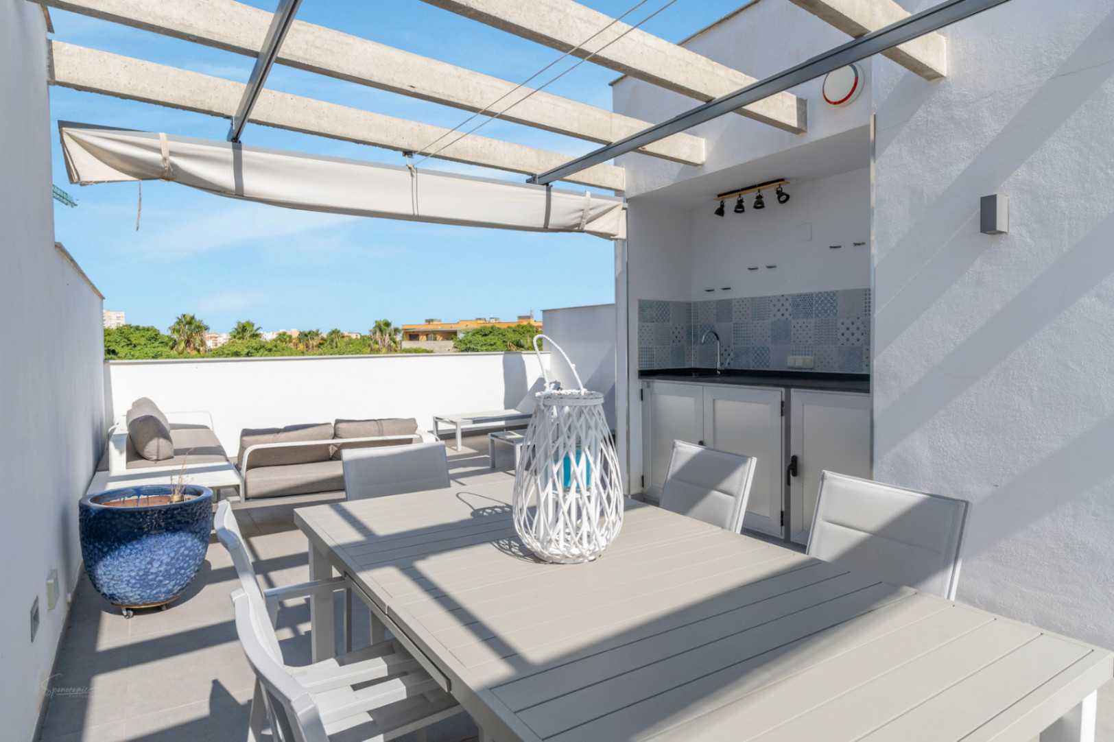 Private Dachterrasse mit integrierter Sommerküche, Essbereich und Lounge unter einer Betonpergola mit ausziehbarer Markise.
