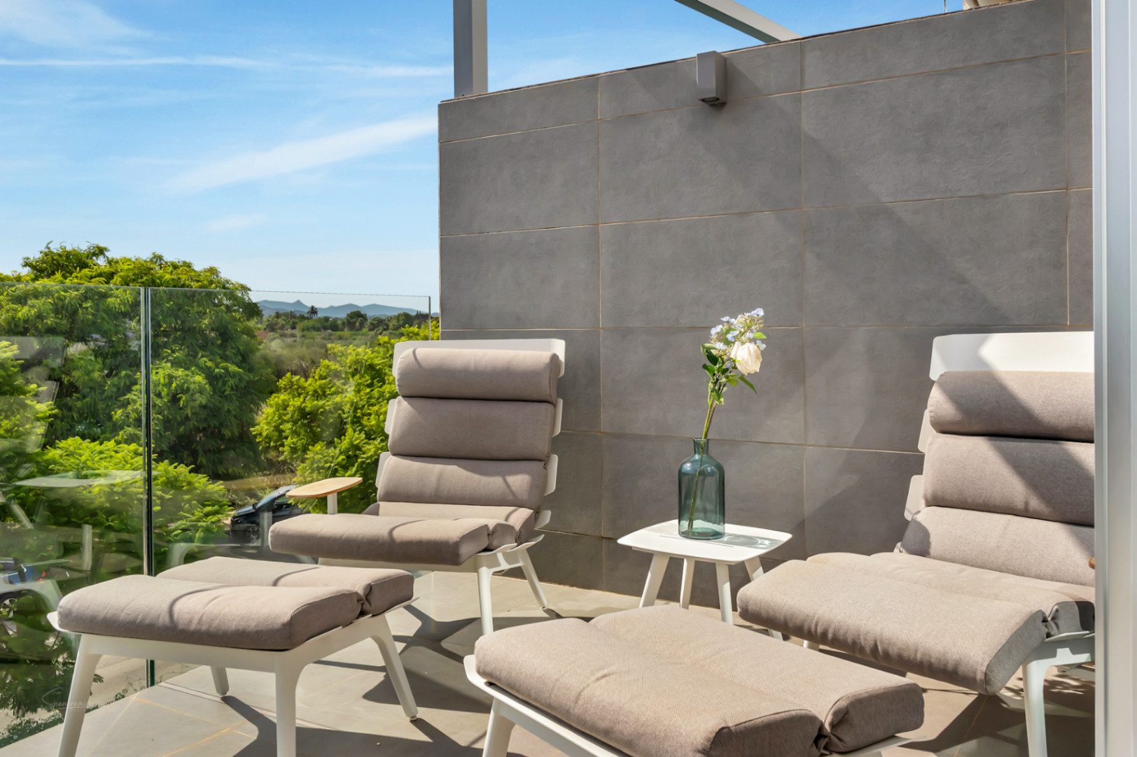 Private Terrasse mit modernen Liegestühlen, Glasgeländer und weitem Blick auf die umliegende Natur und die fernen Berge.