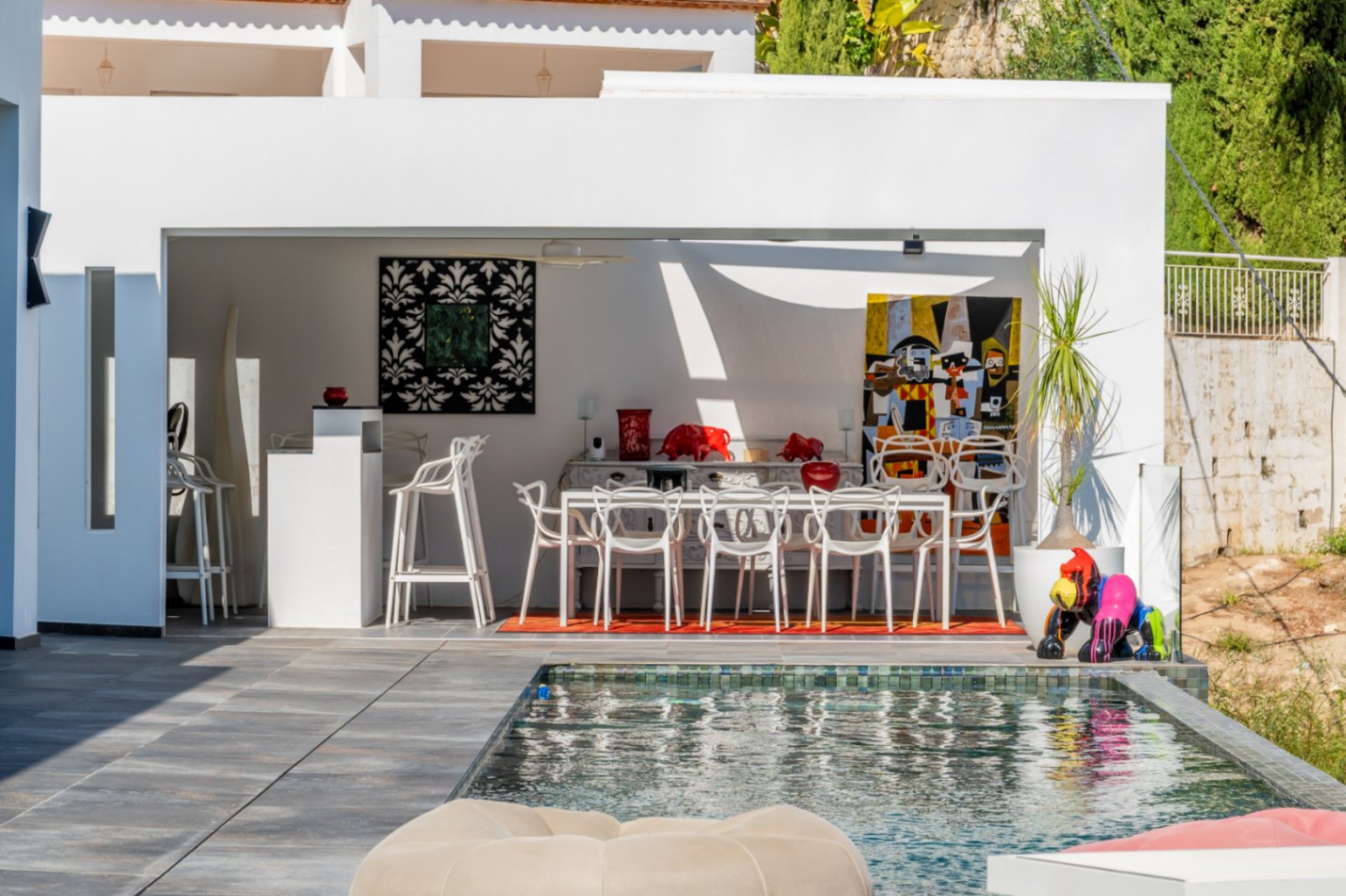 Außenküche und Essbereich am Pool mit weißen Designermöbeln, moderner Kunst und großzügiger Terrasse in minimalistischer Architektur.