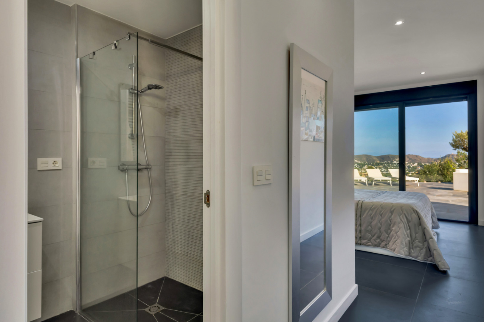 En-Suite-Badezimmer mit begehbarer Glasdusche und grauen Fliesen, das in ein Schlafzimmer mit direktem Zugang zur Terrasse und Bergblick führt.