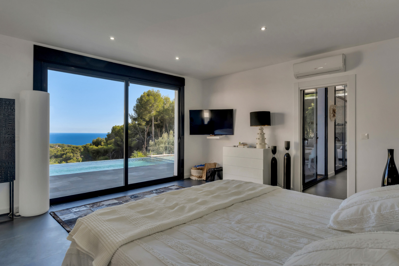 Hauptschlafzimmer mit bodentiefen Glasschiebetüren, die den Blick auf den Infinity-Pool und das Meer freigeben. Mit dunklen Bodenfliesen und integrierter Klimaanlage.
