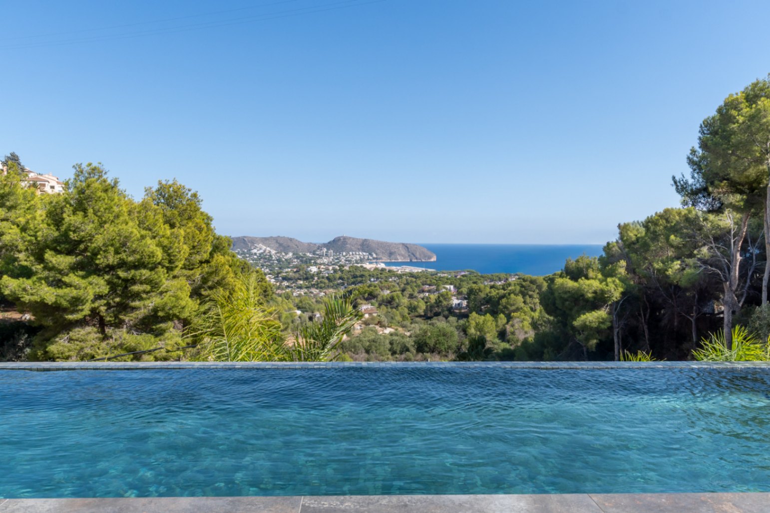 Infinity-Pool mit blauem Mosaik und Panoramablick auf das Mittelmeer, die Küste von Moraira und den umliegenden Pinienwald.