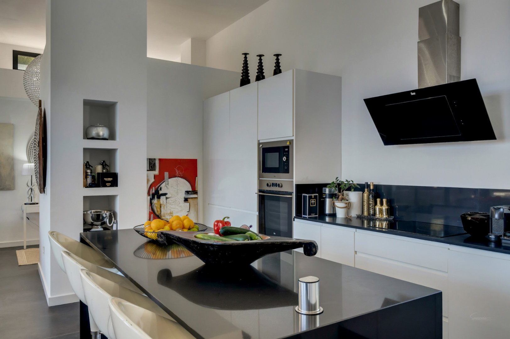 Moderne Küche mit schwarzer Kochinsel, passenden Arbeitsplatten und integrierten Geräten. Minimalistisches Design mit schräger Dunstabzugshaube und Wandeinbauregalen.
