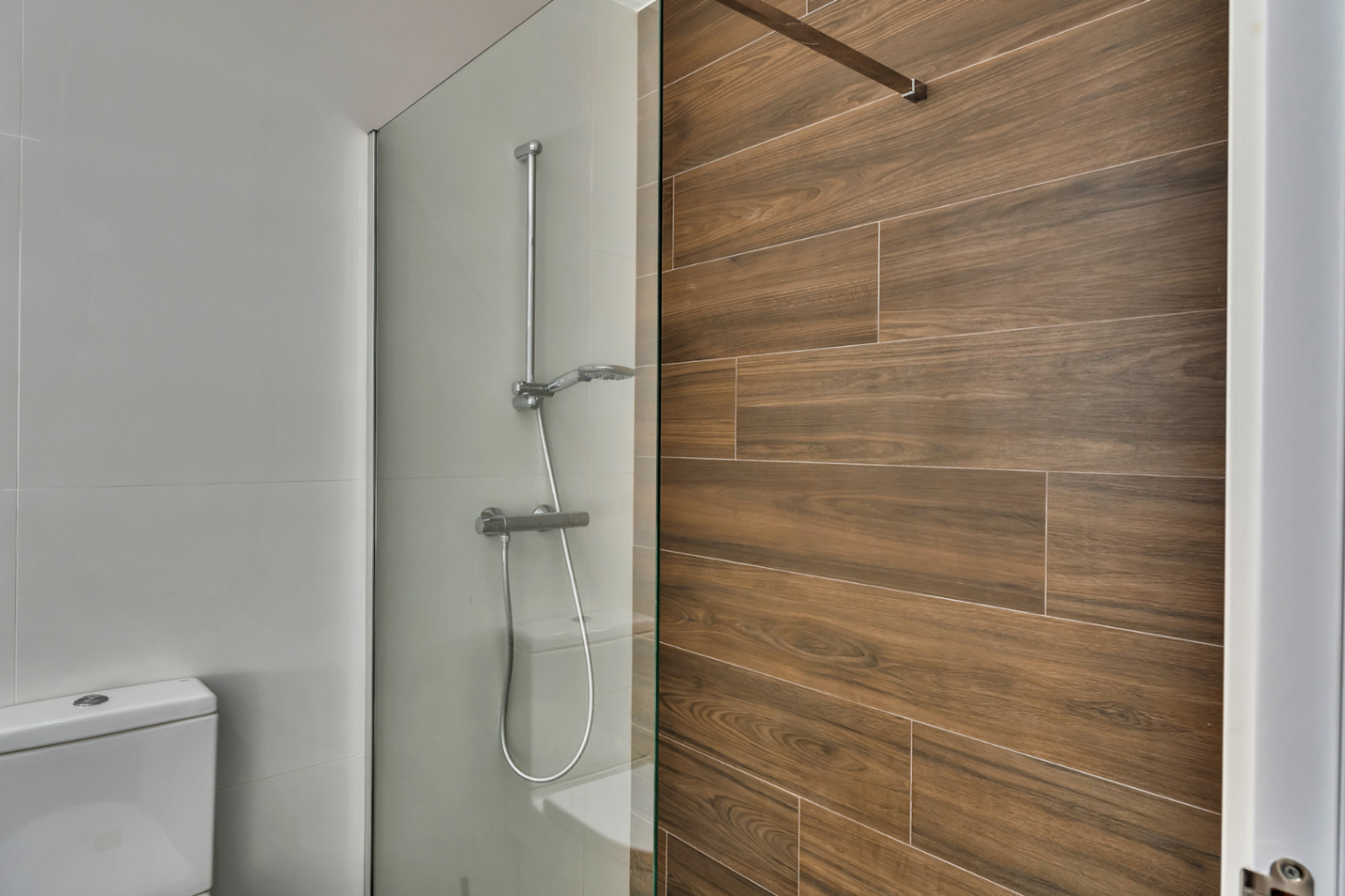 Modernes Badezimmer mit begehbarer Dusche, Glasabtrennung und Wandfliesen in Holzoptik, die einen warmen Akzent zu den weißen Wänden setzen.