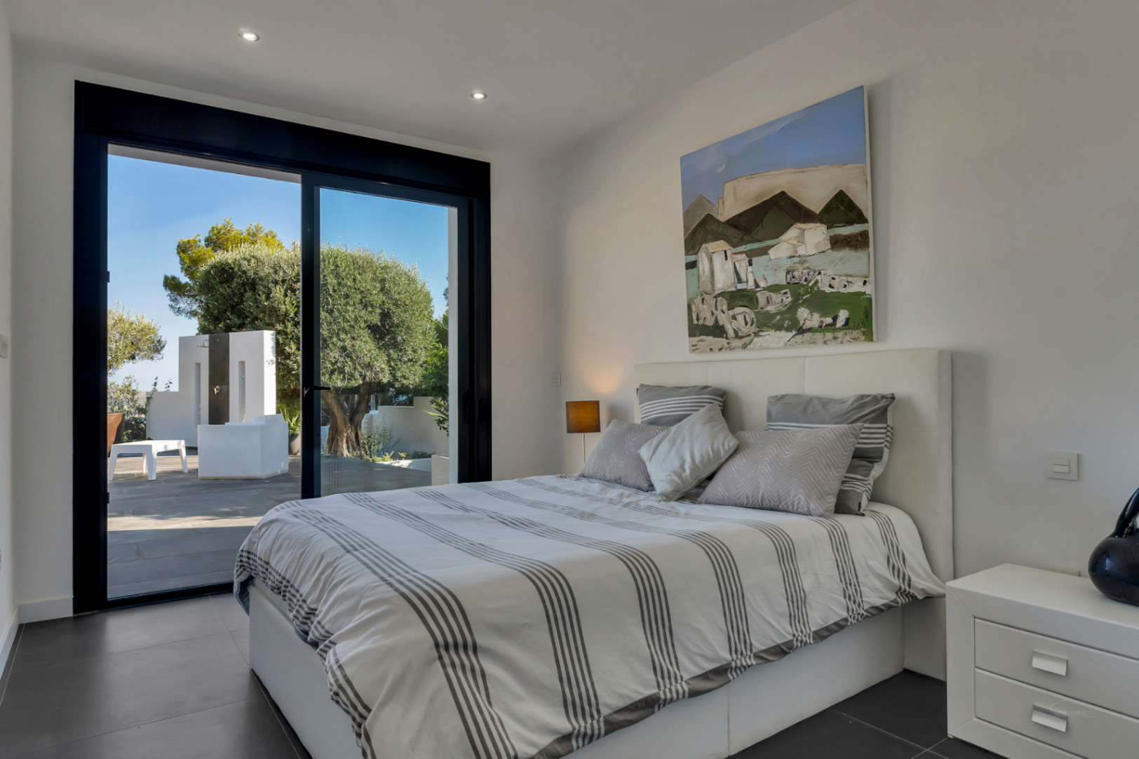 Modernes Schlafzimmer mit direktem Terrassenzugang, schwarzen Schiebefenstern, dunklen Keramikböden und integrierter Deckenbeleuchtung.