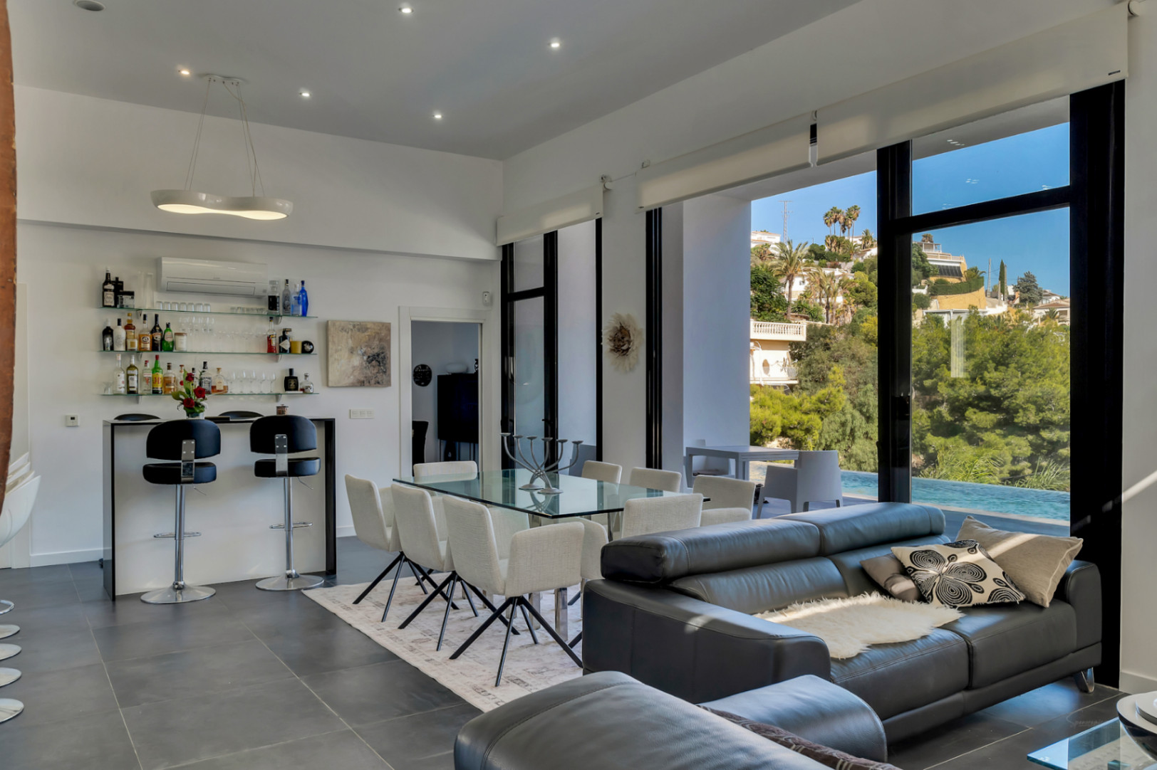 Offener Wohn- und Essbereich mit hohen Decken, integrierter Bar und bodentiefen Fenstern, die den Blick auf den Pool und die mediterrane Landschaft freigeben.