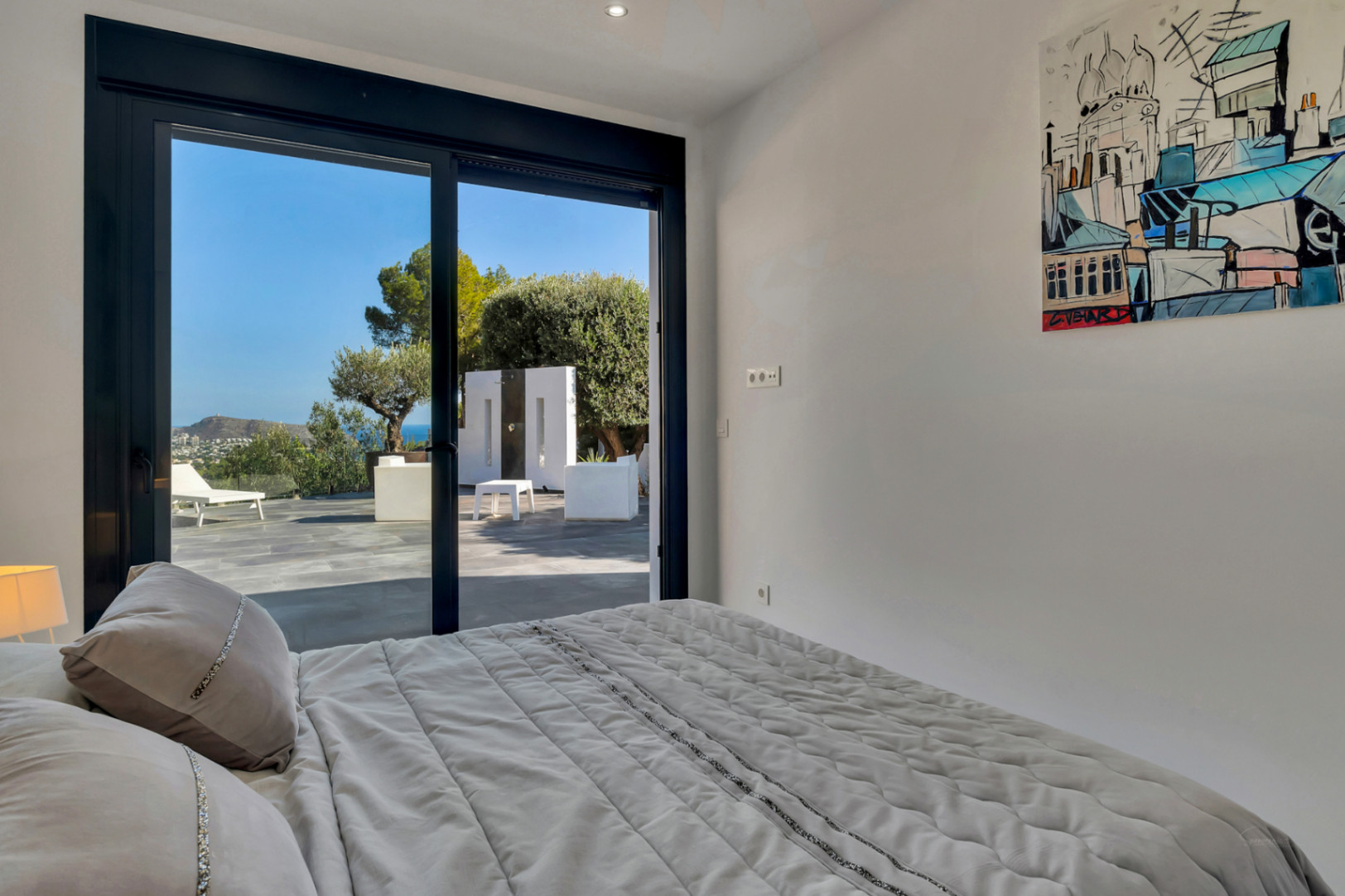 Schlafzimmer mit direktem Terrassenzugang durch bodentiefe Schiebefenster und Blick auf das Mittelmeer und den Garten direkt vom Bett aus.