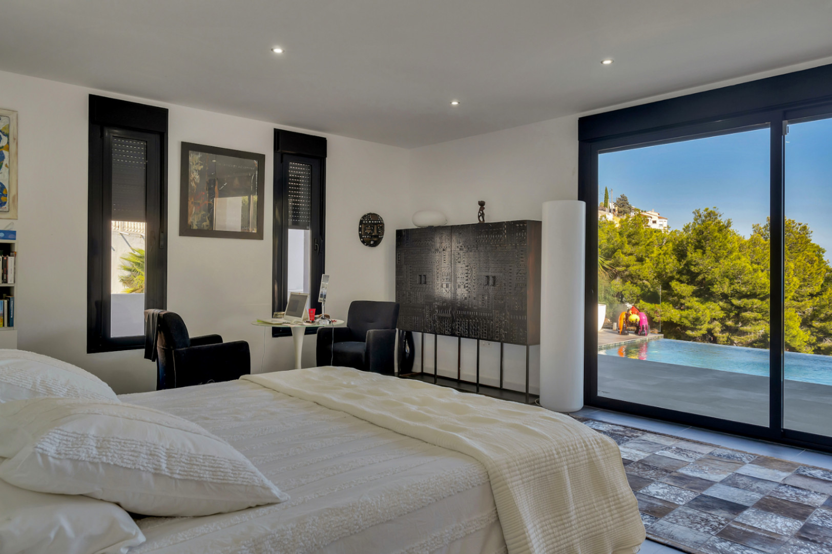 Schlafzimmer mit direktem Zugang zum Pool und zur Terrasse. Es bietet dunkle Designmöbel, Einbaustrahler und einen weiten Blick auf die bewaldete Landschaft.