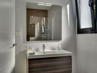 Badezimmerdetail mit modernem Waschbecken und beleuchtetem Spiegel.