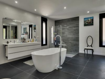 Helles Badezimmer mit freistehender Badewanne, Waschtisch mit Spiegel und grauem Fliesenboden.