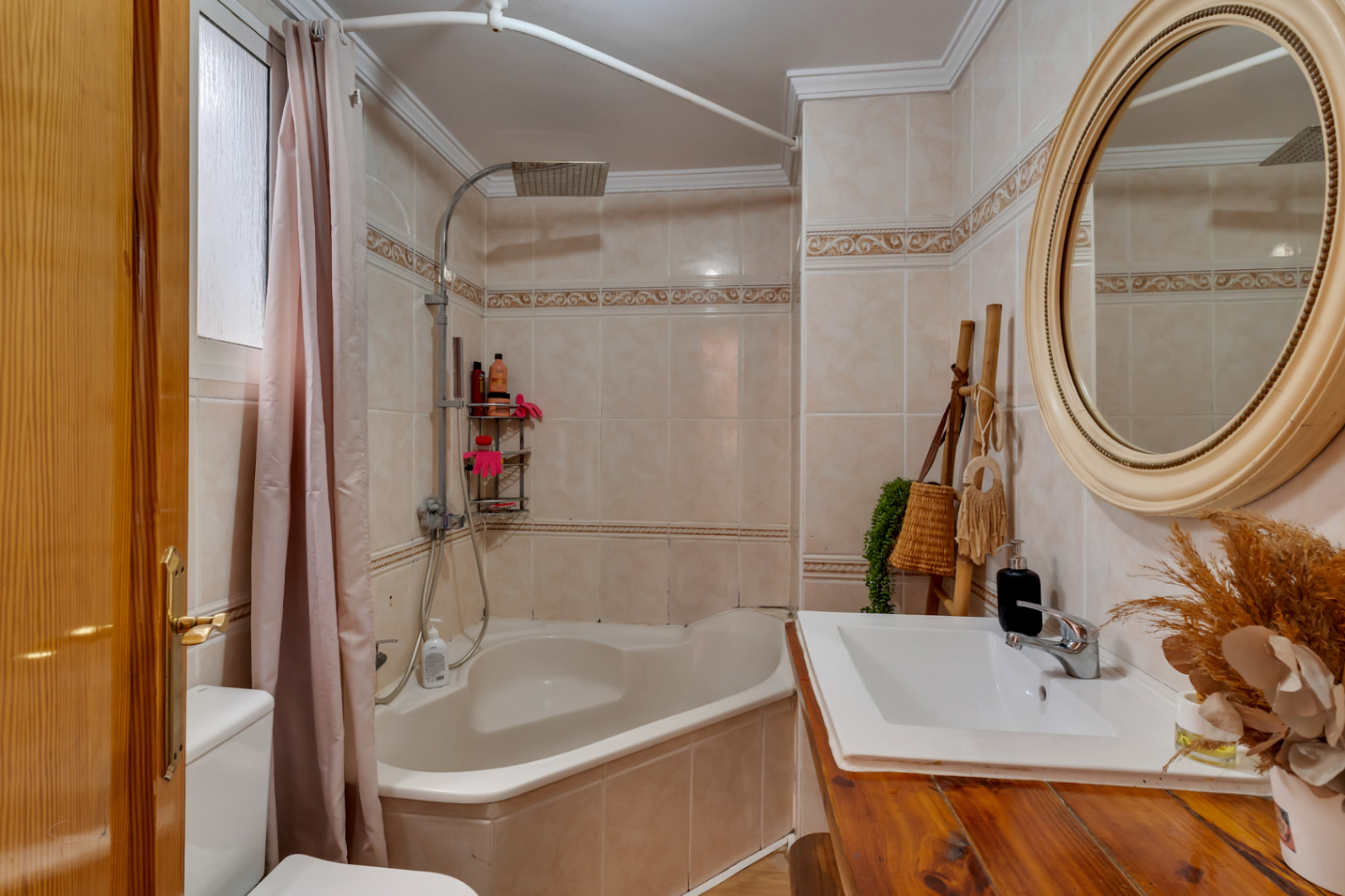 Badezimmer mit Eckbadewanne, Regendusche und rustikalem Holzwaschtisch vor cremefarbenen Fliesen mit dekorativer Bordüre.