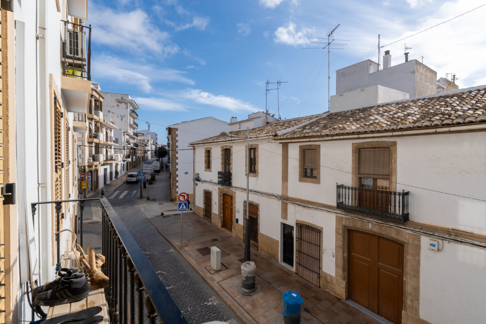 Blick vom Balkon auf eine Straße in der Altstadt von Jávea mit traditionellen weißen Fassaden, Ziegeldächern und architektonischen Details aus Naturstein.