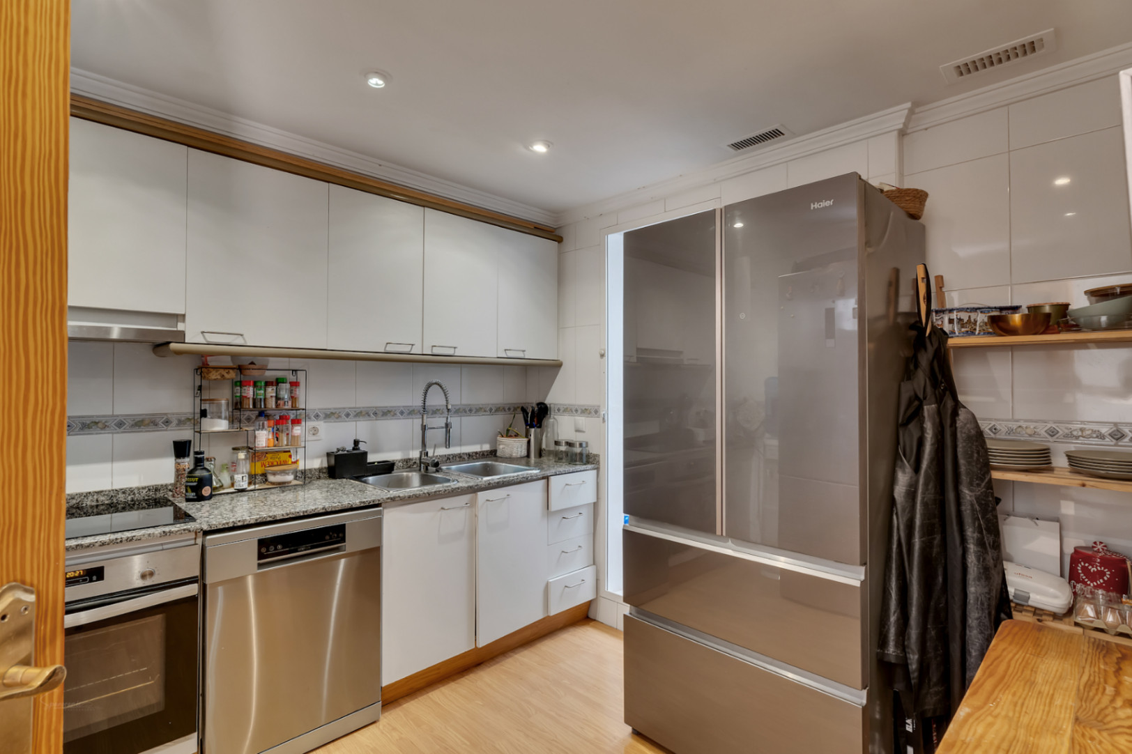 Funktionale Küche mit weißen Schränken, Granitarbeitsplatte und Edelstahlgeräten, ausgestattet mit einem großen Side-by-Side-Kühlschrank und integriertem Geschirrspüler.