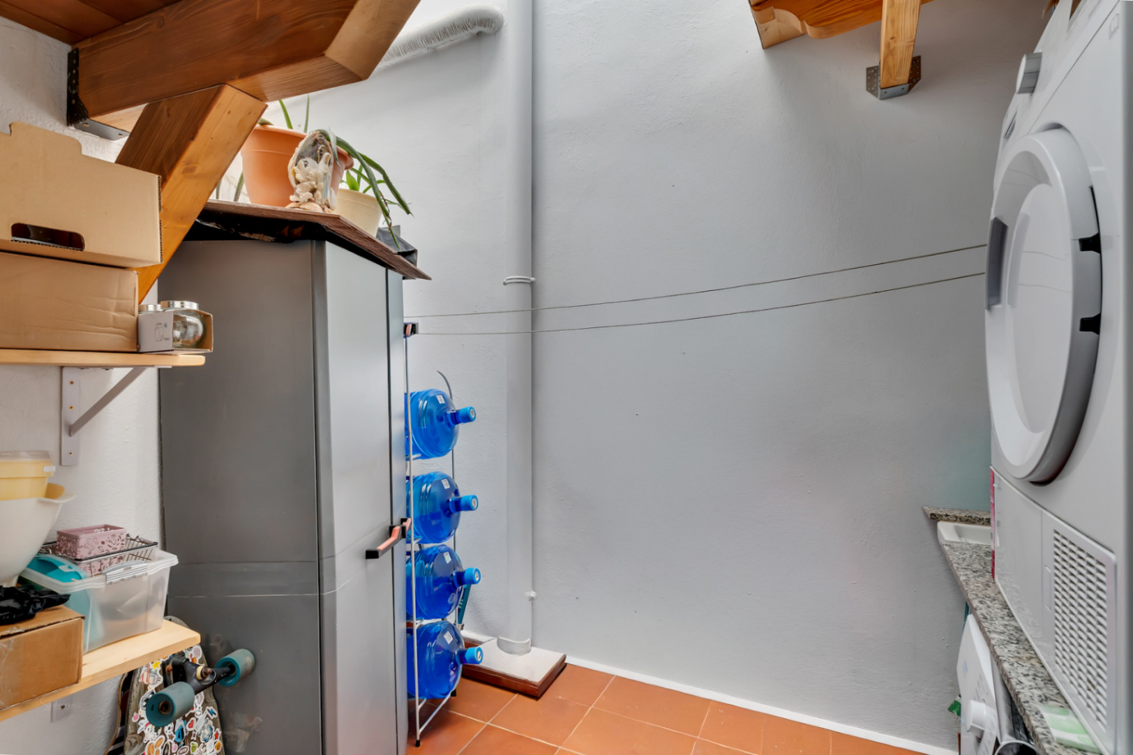 Funktionaler Innenhof mit Waschbereich, Terrakottaboden, Holzbalken und organisierten Aufbewahrungsmöglichkeiten.