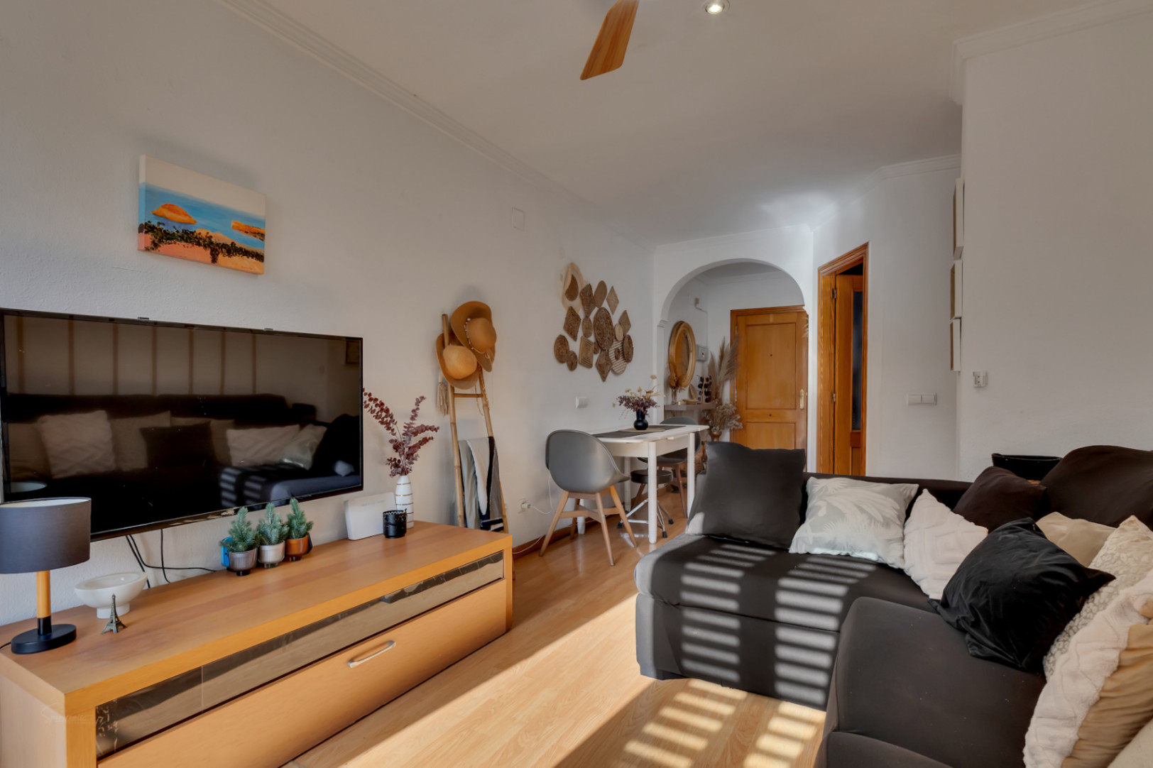 Heller Wohn- und Essbereich mit Parkettboden, dunklem Sofa und TV-Möbel. Mit Essecke unter einem Rundbogen und Dekoration im mediterranen Stil.
