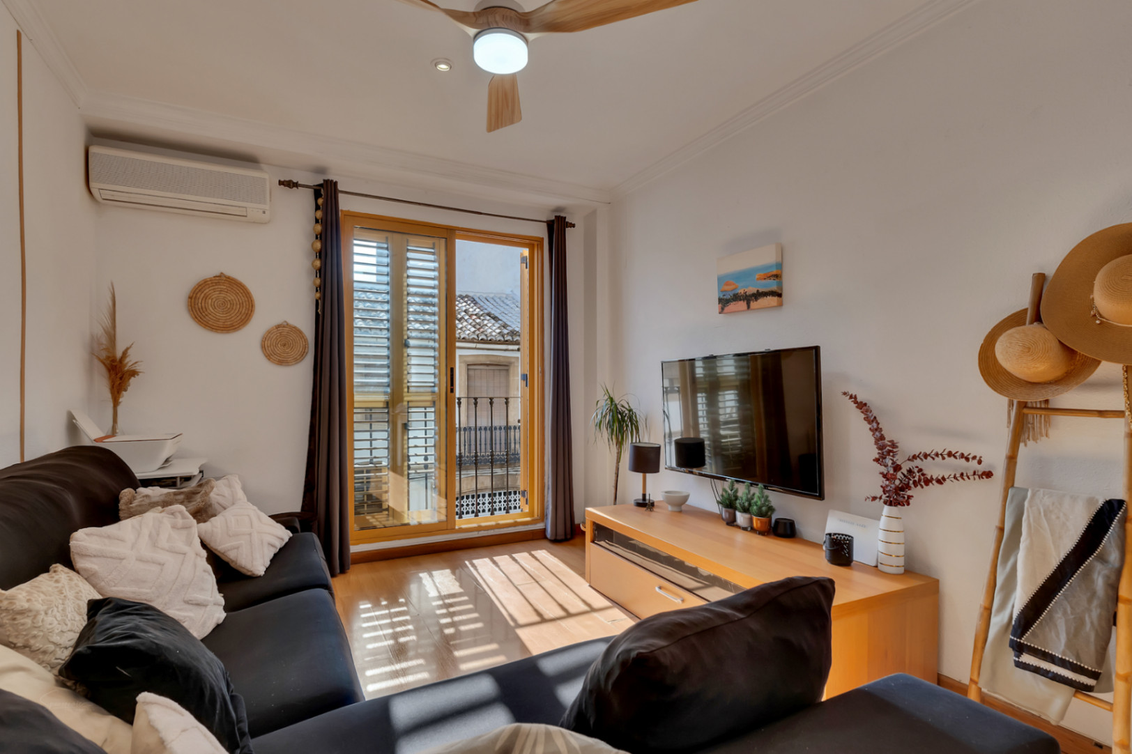 Heller Wohnbereich mit Parkettboden, Klimaanlage und Zugang zum Balkon mit Holzschlagläden. Ausgestattet mit Deckenventilator und funktionalem TV-Möbel.