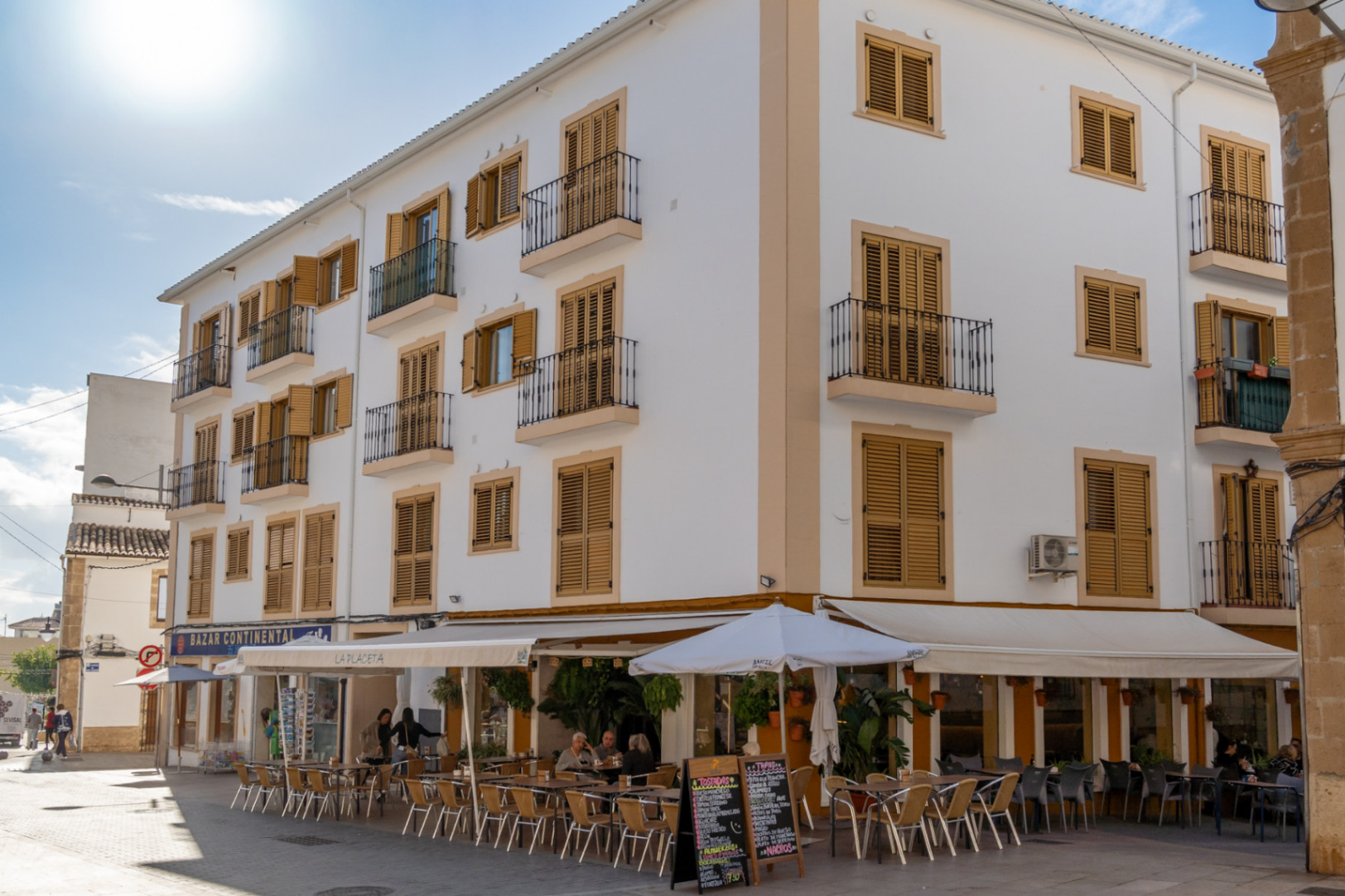 Traditionelle Fassade im historischen Zentrum mit ockerfarbenen Holzfensterläden, schmiedeeisernen Balkonen und einem Straßencafé in der Fußgängerzone.