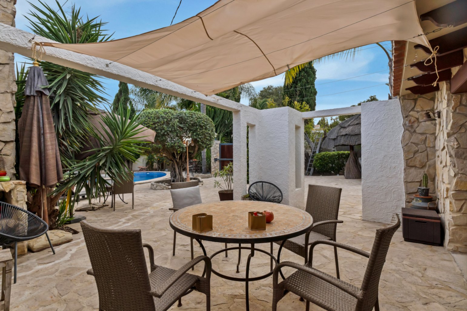Außen-Terrasse mit Natursteinboden, Mosaiktisch unter einem Sonnensegel und Blick auf den privaten Pool und den mediterranen Garten.