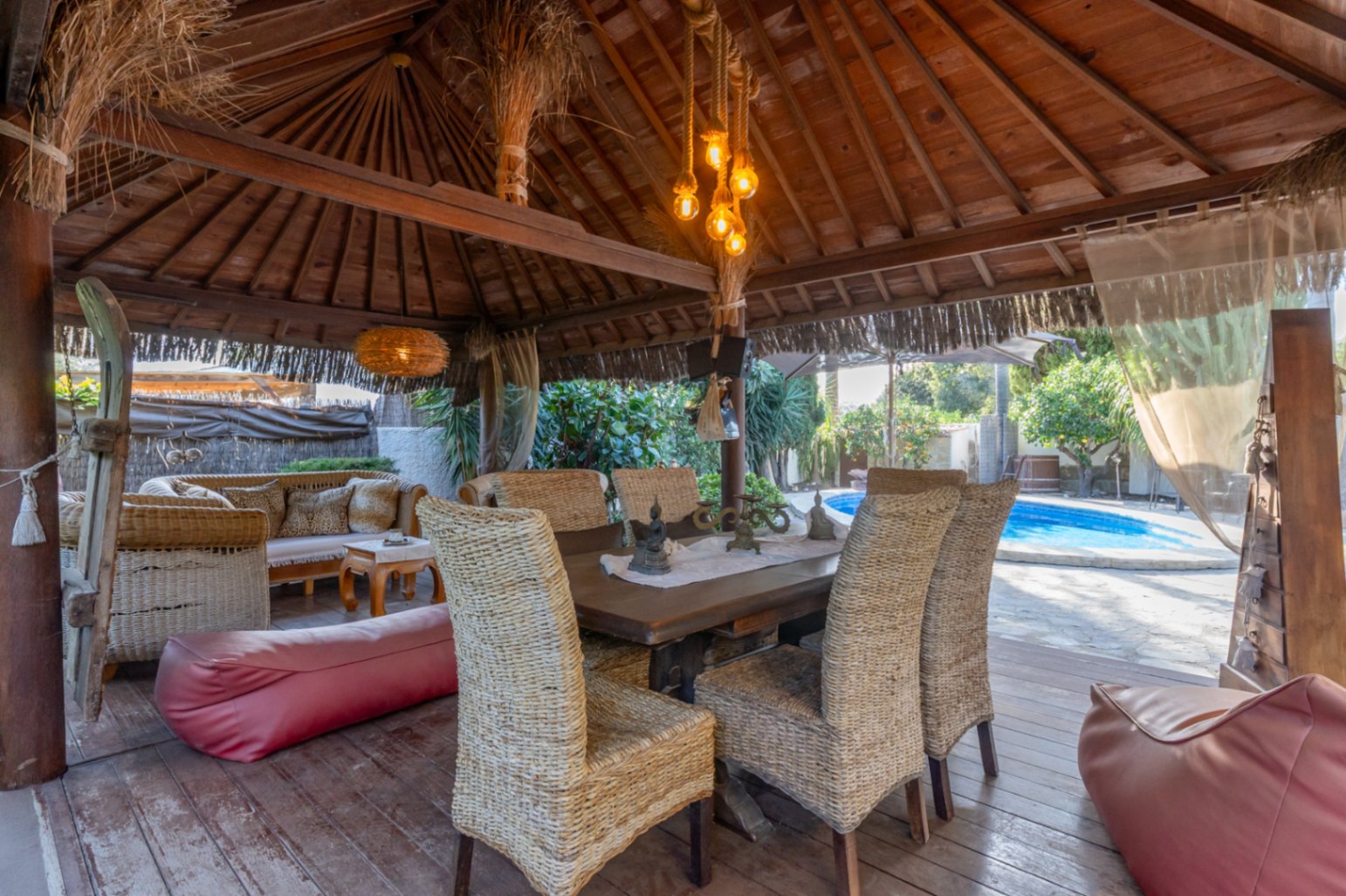 Holzpergola im balinesischen Stil mit Außen-Essbereich, Korbstühlen und Blick auf den privaten Pool und den Garten.