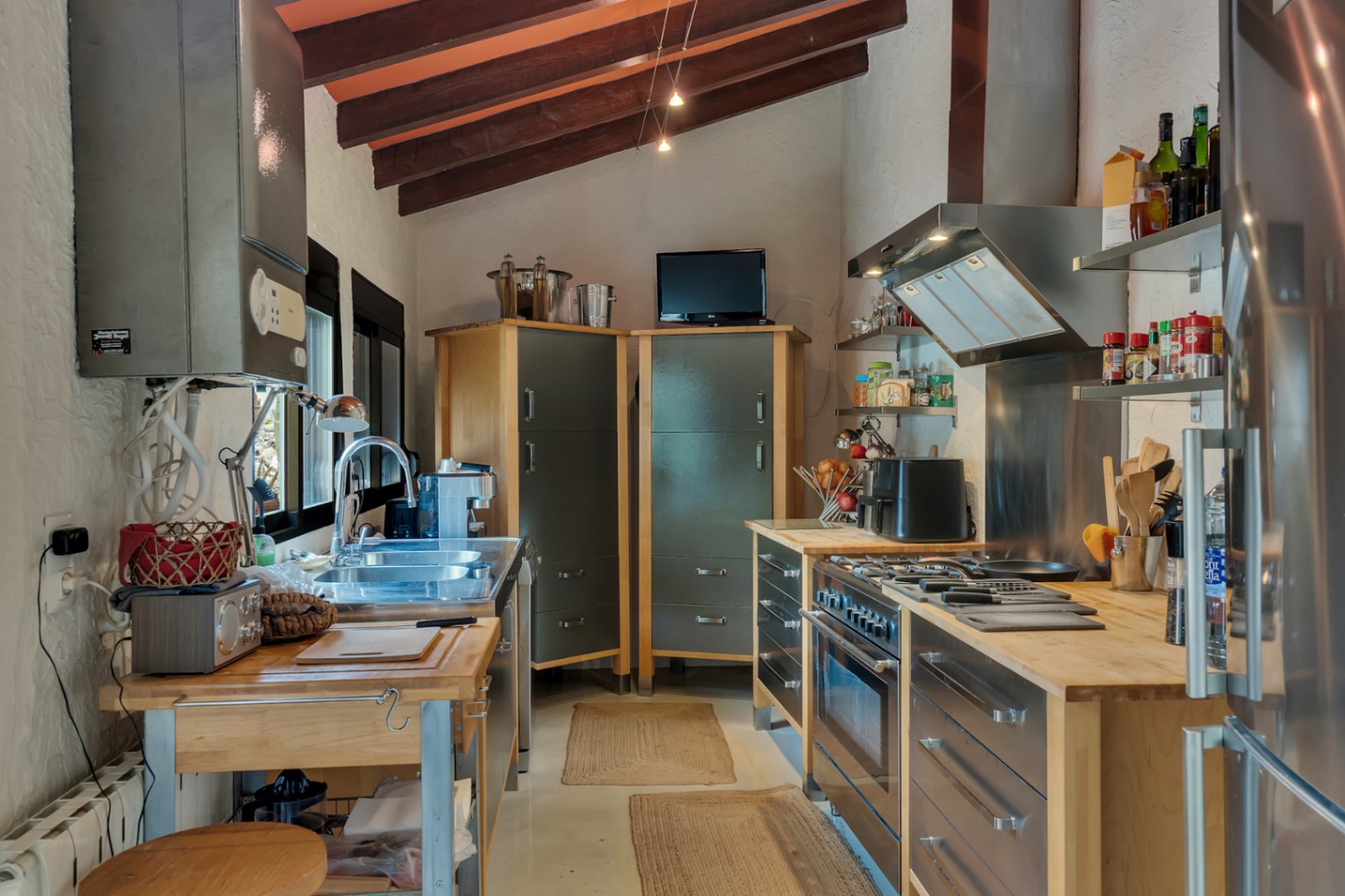 Küche im Industriestil mit sichtbaren Holzbalken, Massivholz-Arbeitsplatten und Edelstahlgeräten in einem funktionalen Raum mit Dachschräge.
