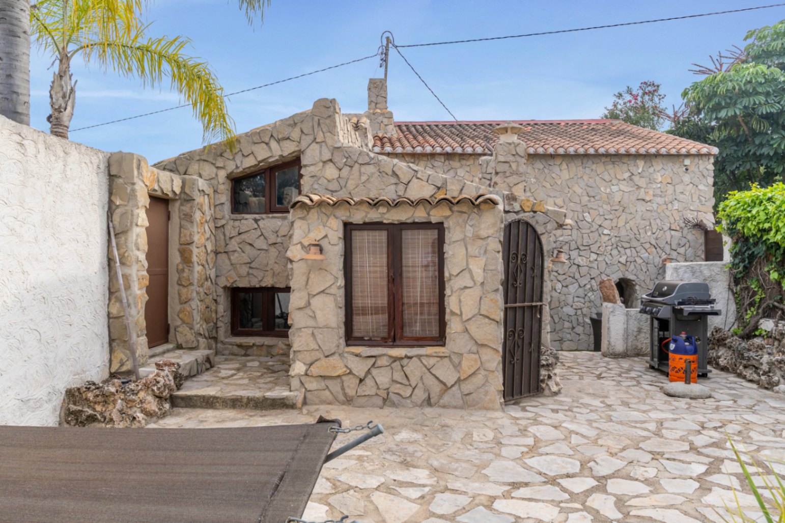 Natursteinfassade mit dunklen Holzfensterrahmen und gepflastertem Innenhof. Der Außenbereich bietet einen Grillplatz und traditionelle mediterrane Steinmetzarbeit.