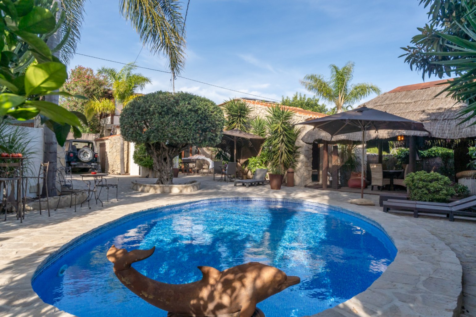 Privater Poolbereich mit Naturstein-Terrasse, mediterraner Bepflanzung und einer balinesischen Pergola mit Reetdach in ruhiger Gartenatmosphäre.