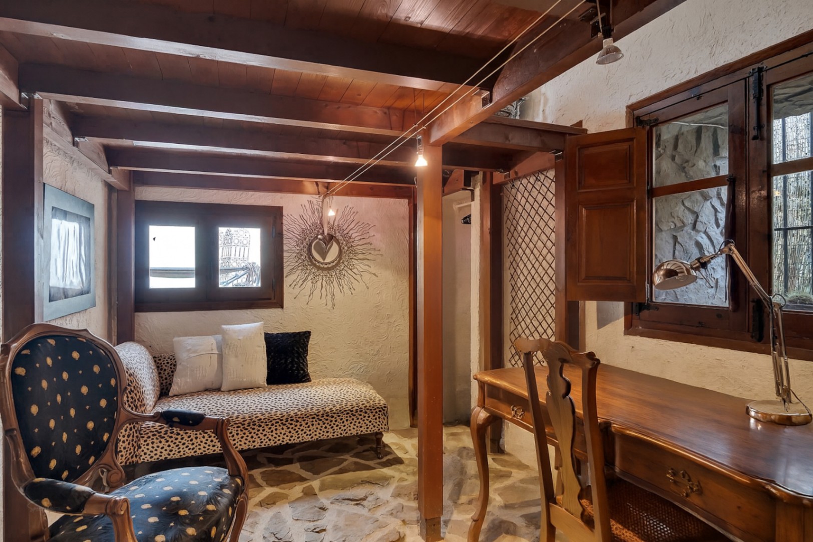 Rustikales Arbeitszimmer mit sichtbaren Holzbalken, Natursteinboden, klassischem Holzschreibtisch und einer Chaiselongue im Leopardenmuster.