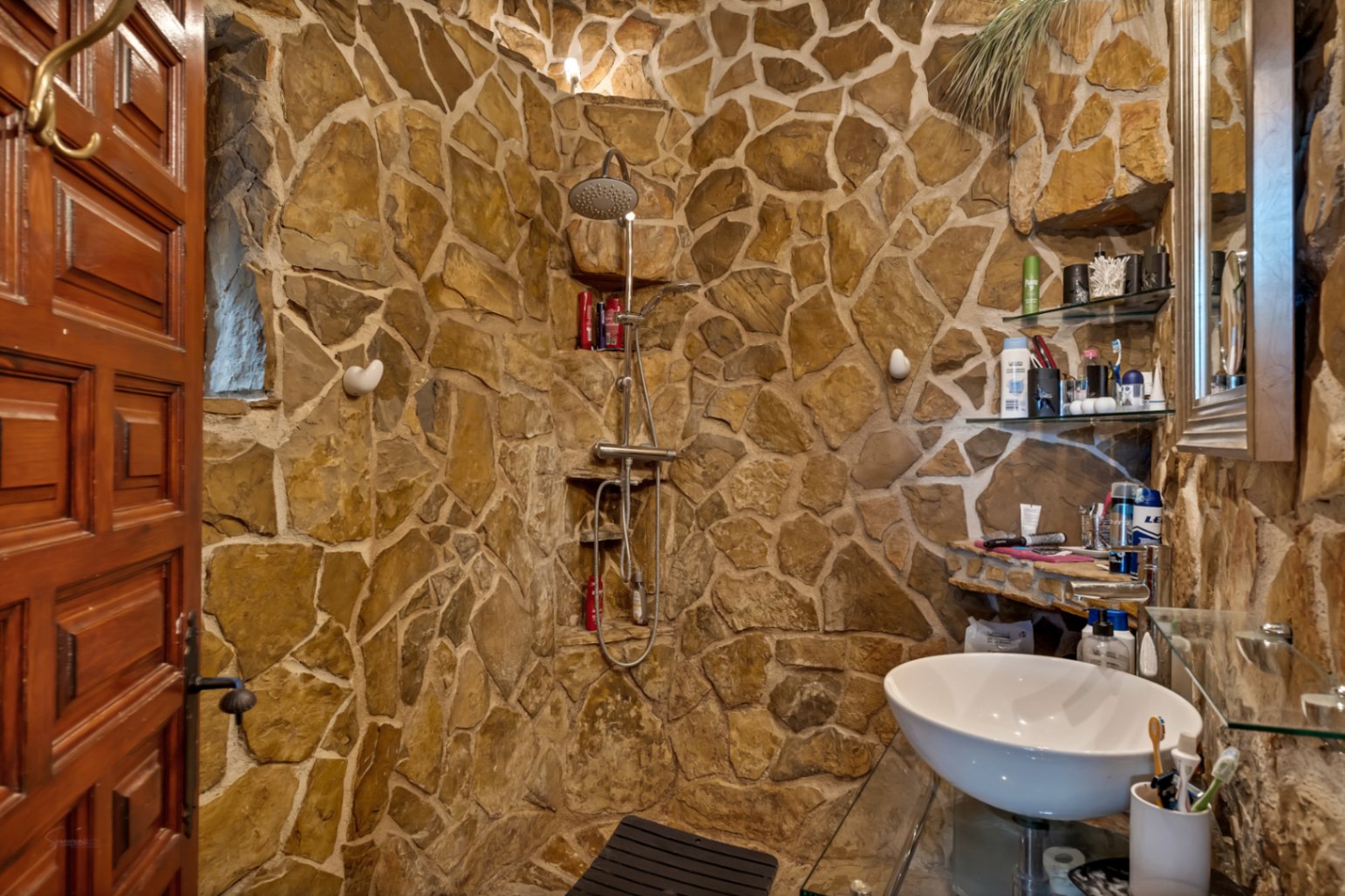 Rustikales Badezimmer mit Natursteinwänden, einer begehbaren Dusche mit Edelstahlarmaturen und einem modernen Aufsatzwaschbecken auf Glasplatte.