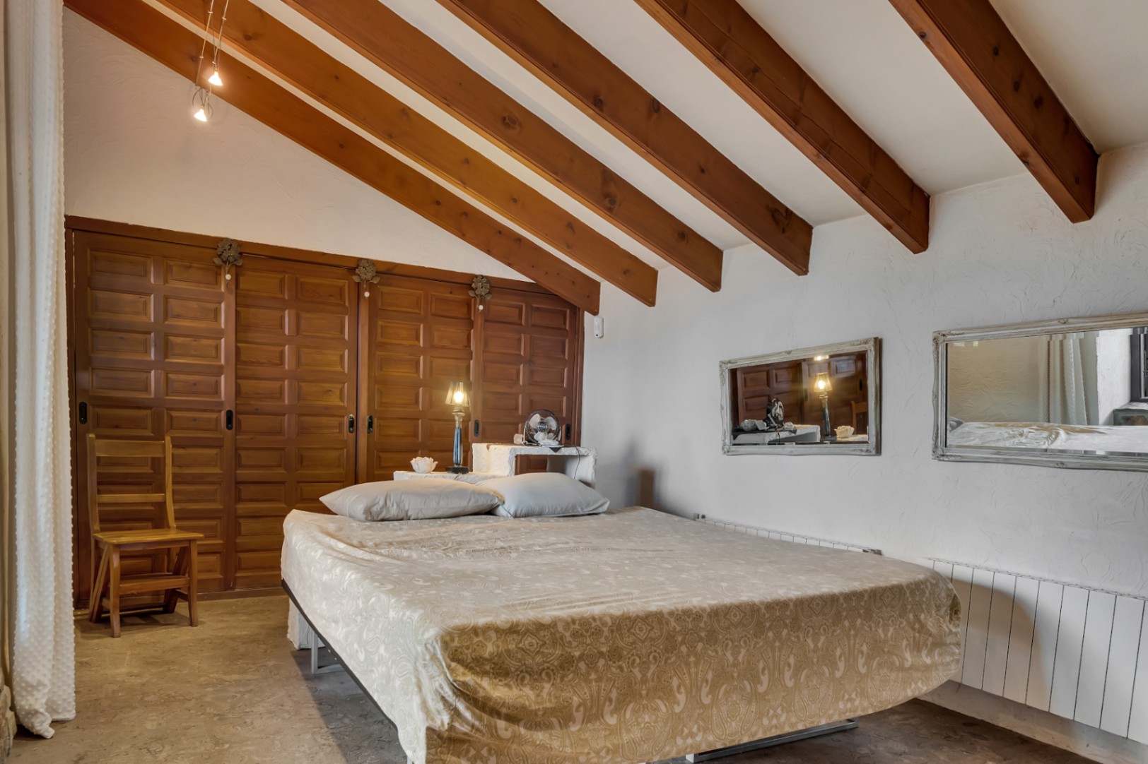 Schlafzimmer mit Dachschräge und sichtbaren Holzbalken, großen Einbauschränken aus Holz und strukturierten weißen Wänden.