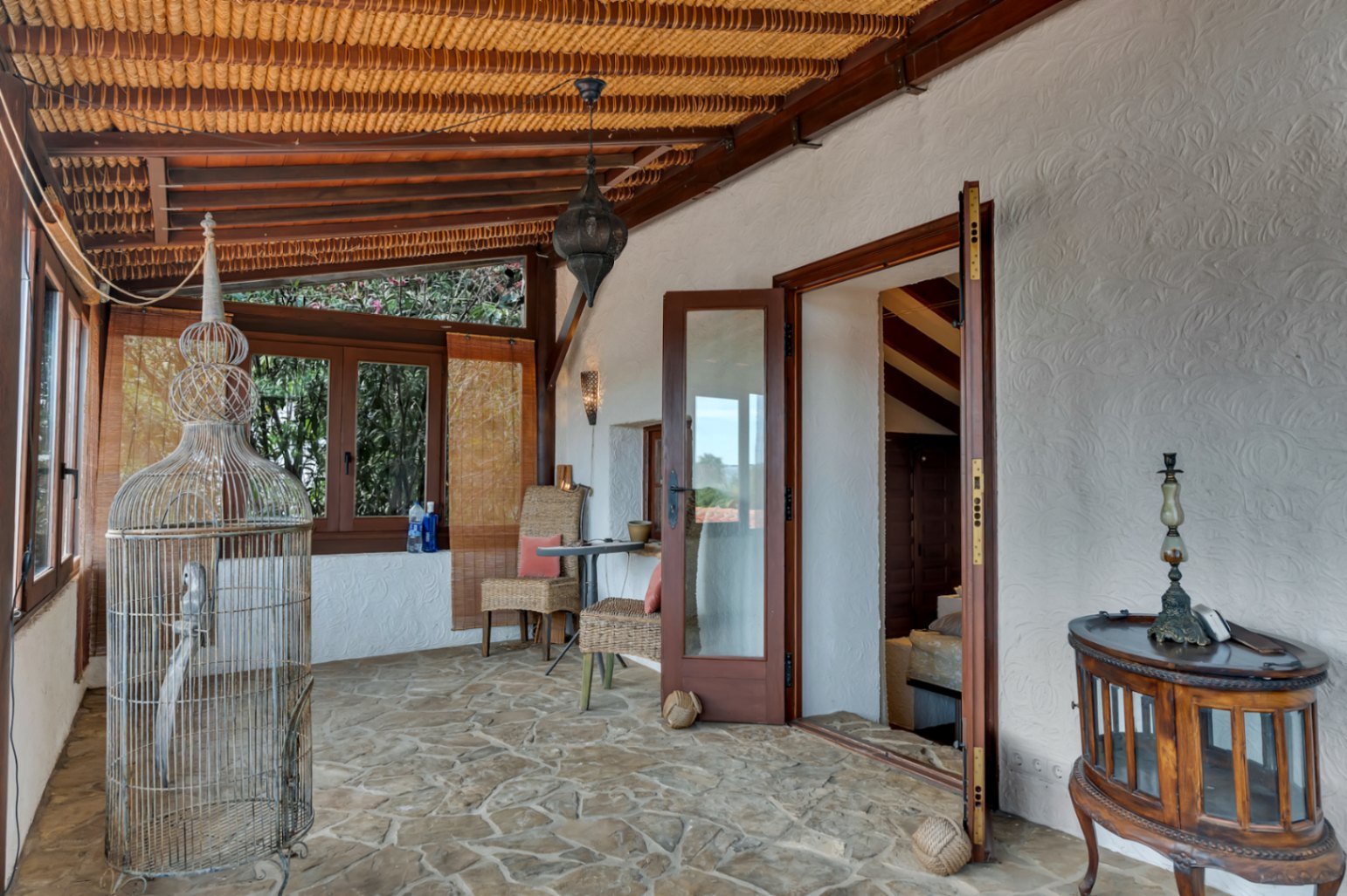 Traditionelle Naya mit Natursteinboden, Holzbalkendecke mit Schilfrohr und Korbmöbeln. Große Glastüren führen direkt in die Innenräume der Villa.