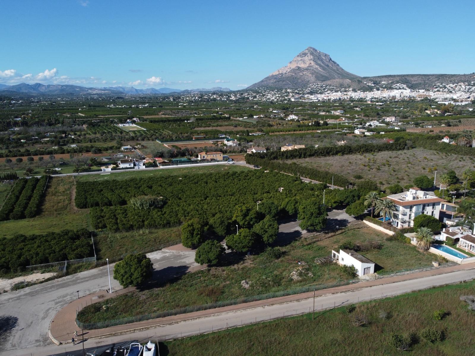 Luftaufnahme des erschlossenen Grundstücks mit asphaltierter Zufahrt, umgeben von Grünflächen und mit Blick auf das markante Montgó-Massiv.