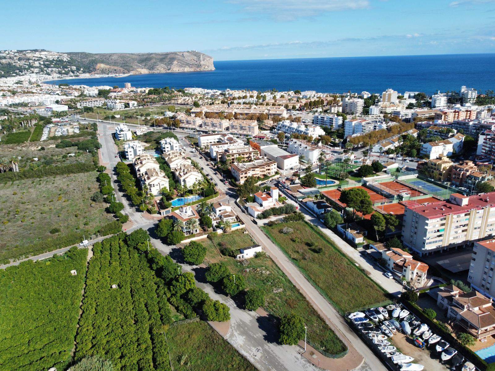 Luftbild des rechteckigen Grundstücks neben landwirtschaftlichen Flächen mit Blick auf den Tennisclub und die Bucht von Jávea im Hintergrund.