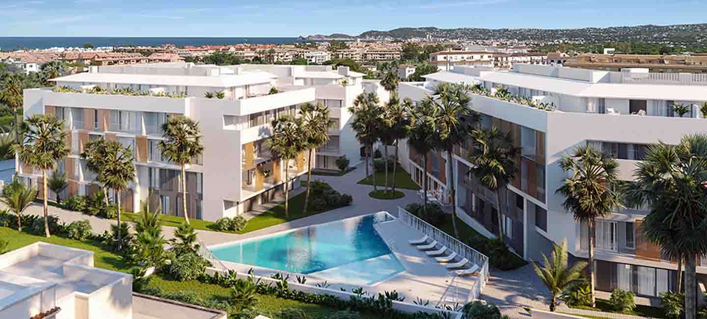Luftaufnahme der modernen Apartmentanlage mit weißen Gebäuden, Holzläden, einem dreieckigen Pool und angelegten Gärten mit Palmen.