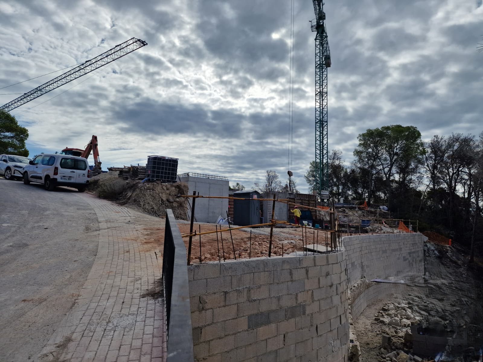 Aktueller Baustand in Moraira mit geschwungenen Stützmauern, gepflasterter Zufahrt und schweren Baumaschinen während der ersten Strukturphase des Projekts.