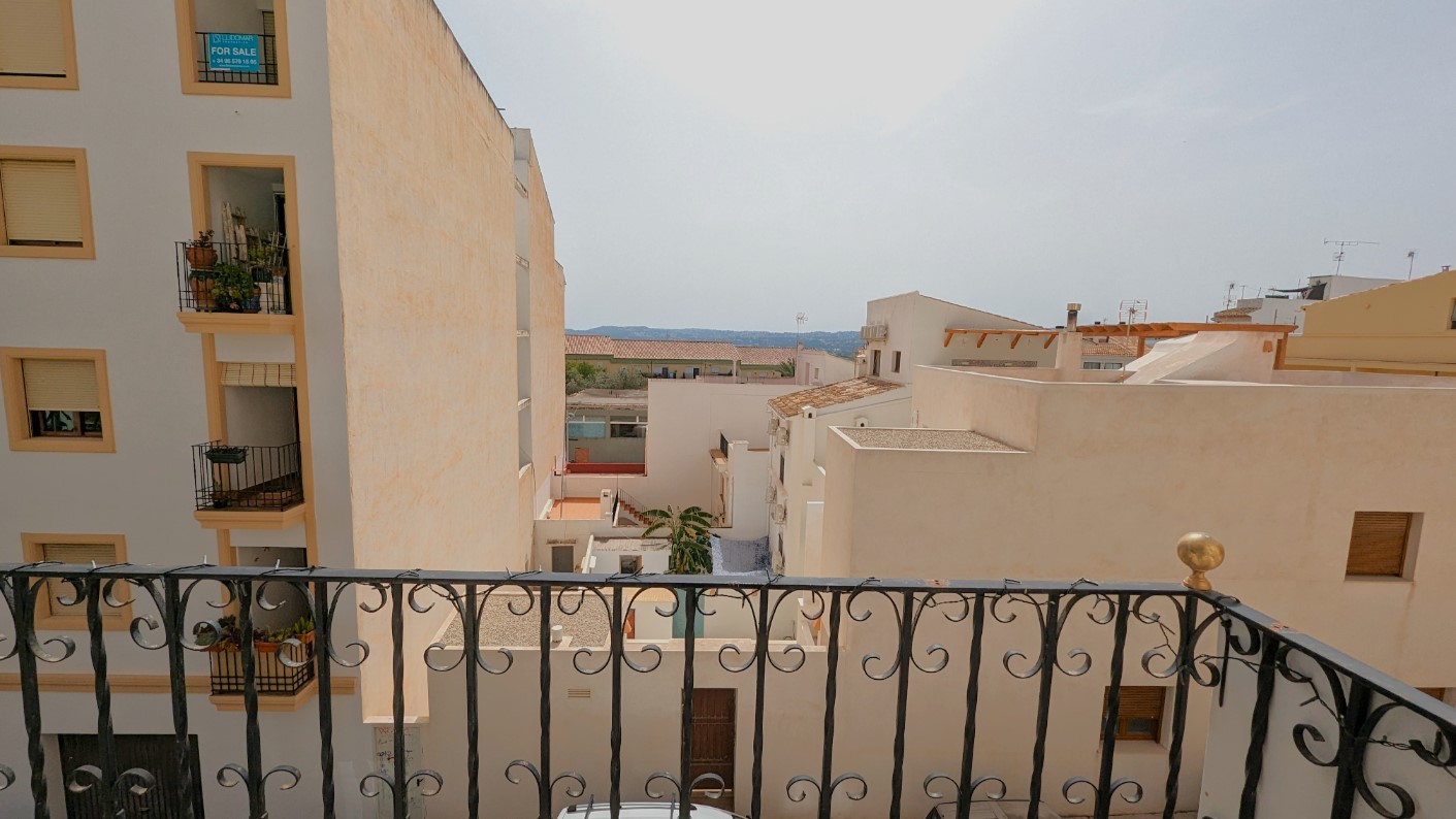Blick vom Balkon mit schmiedeeisernem Geländer über die Dächer der Altstadt von Javea bis hin zum bergigen Horizont in der Ferne.