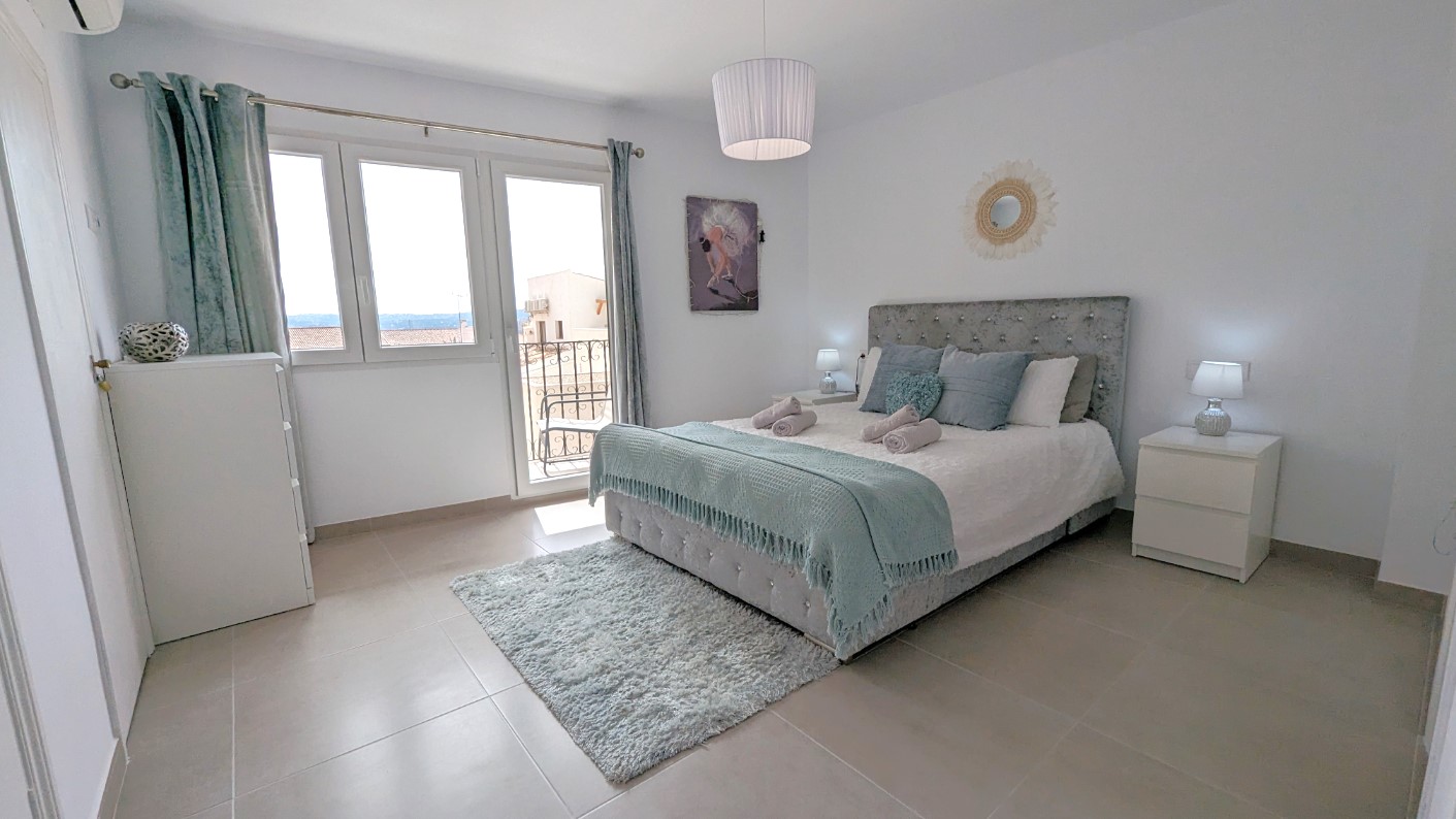 Hauptschlafzimmer mit gepolstertem Kopfteil, Zugang zur privaten Terrasse durch Glastüren und hellen Bodenfliesen in modernem Design.