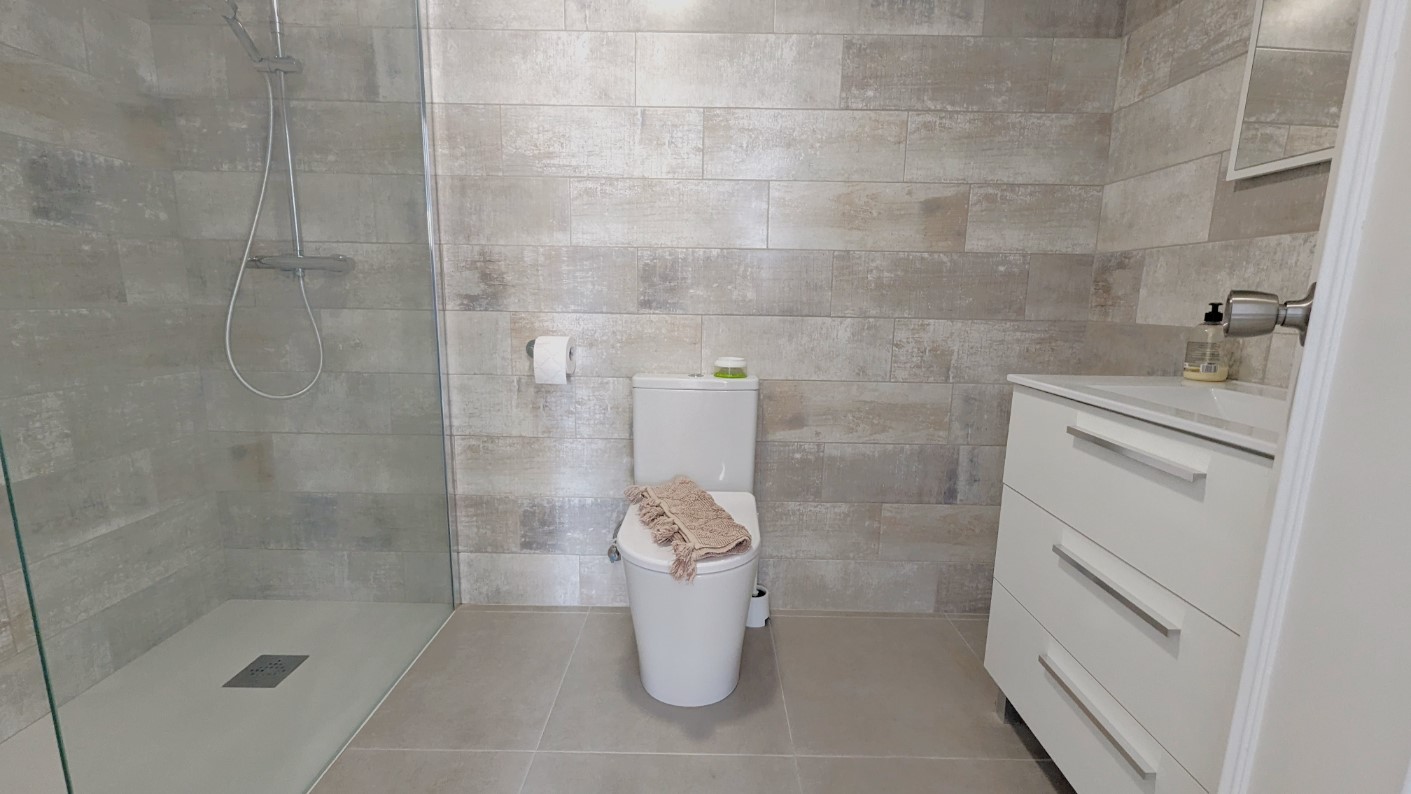 Modernes Badezimmer mit begehbarer Dusche, Glastrennwand, strukturierten grauen Wandfliesen und einem weißen Waschtisch mit Schubladen.