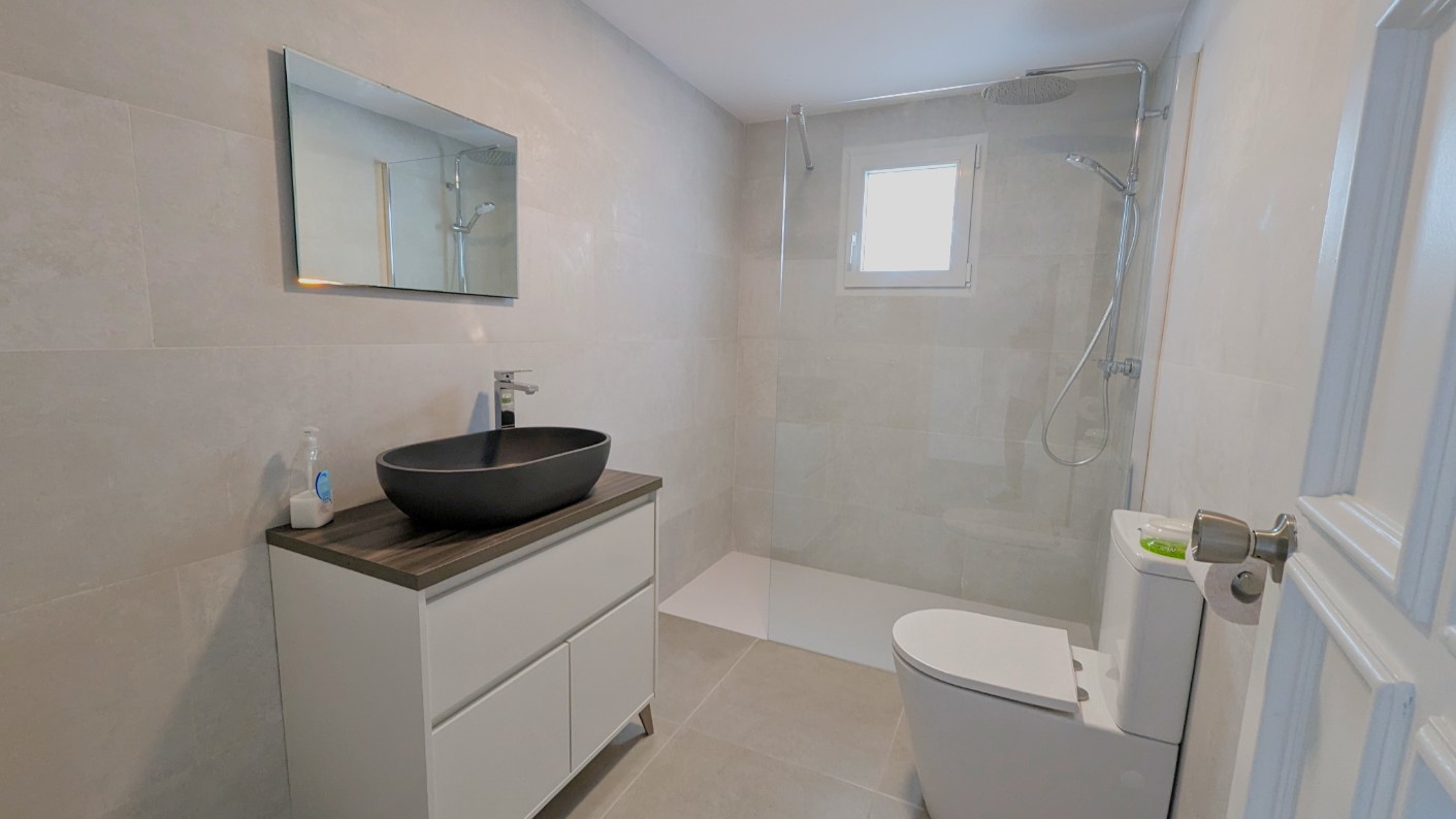 Modernes Badezimmer mit schwarzem Aufsatzwaschbecken, begehbarer Dusche mit Glastrennwand und großformatigen grauen Wand- und Bodenfliesen.