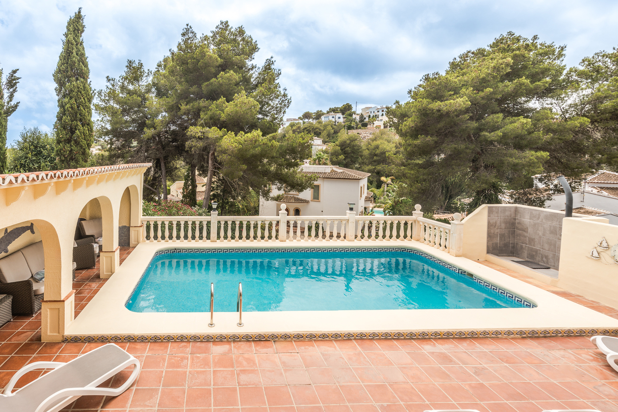 Außenanlage mit 8x4m Pool, weißer Balustrade und einer überdachten Rundbogenterrasse, eingebettet in einen Garten mit altem Kiefernbestand.