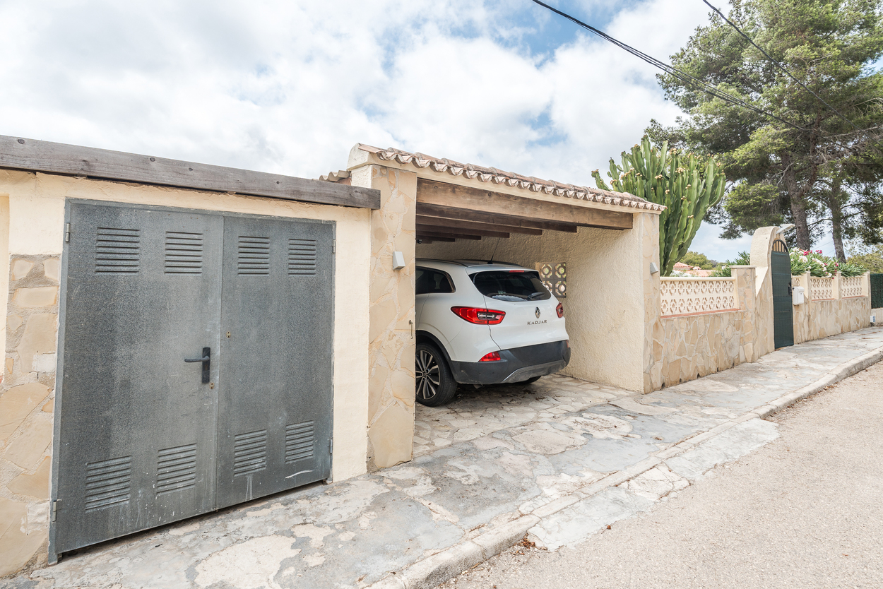 Außenansicht mit ummauertem Eingang, Natursteinwänden und einem überdachten Carport mit Holzbalken für sicheres Parken auf dem Grundstück.
