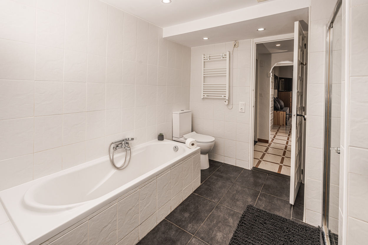 Funktionales Badezimmer mit weiß gefliester Badewanne, dunklem Fliesenboden, Handtuchheizkörper und Deckeneinbaustrahlern.