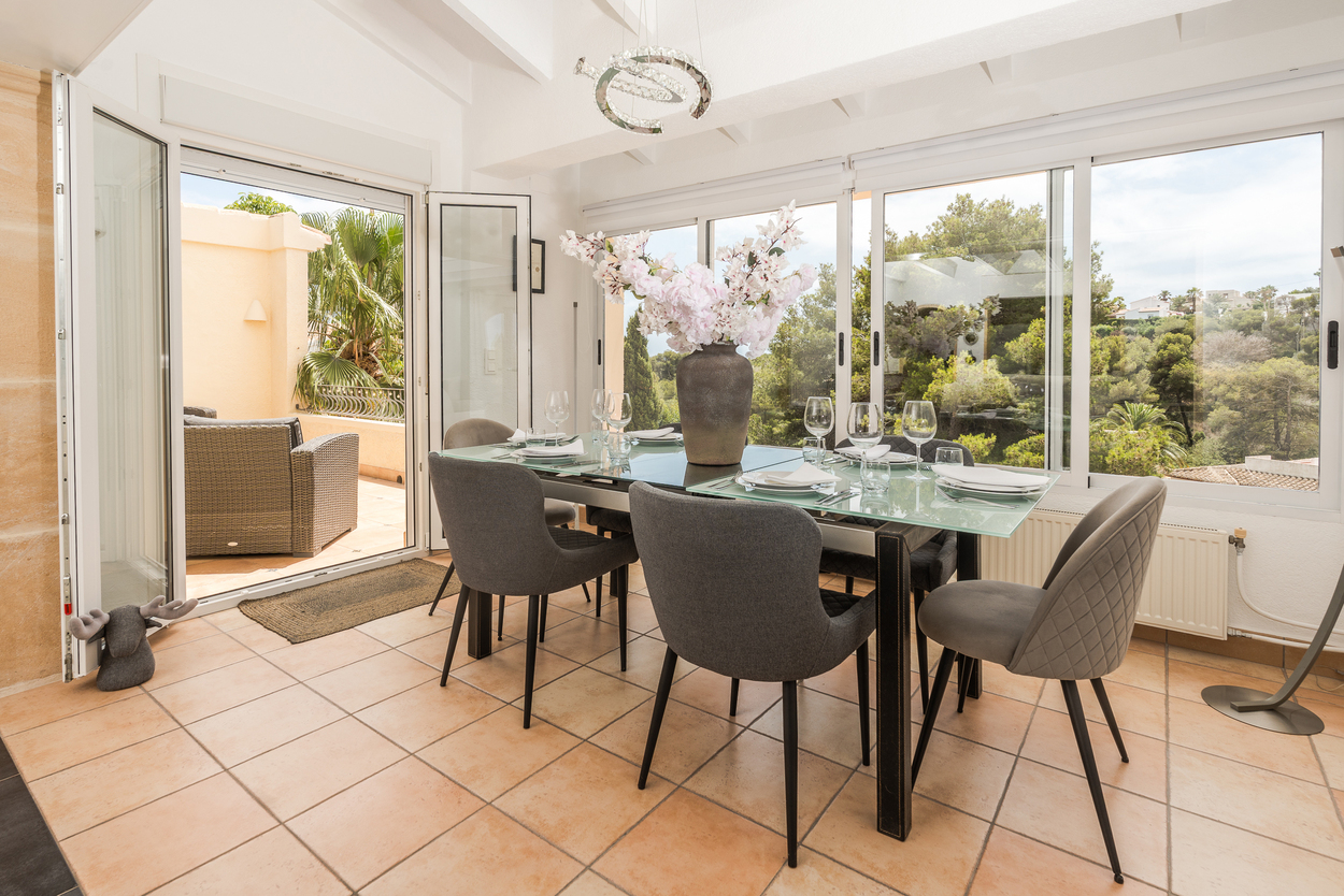 Heller Essbereich mit Terrakottaboden, weißen Balkendecken und großen Glastüren, die auf eine Terrasse mit Blick auf die mediterrane Landschaft führen.