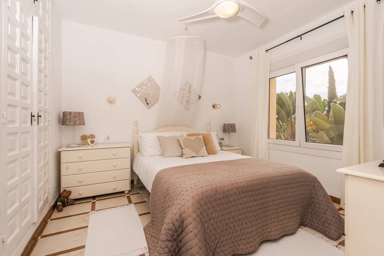 Helles Schlafzimmer mit Einbauschränken, Deckenventilator und doppelt verglasten Fenstern mit Blick ins Grüne sowie einem traditionellen Fliesenboden.