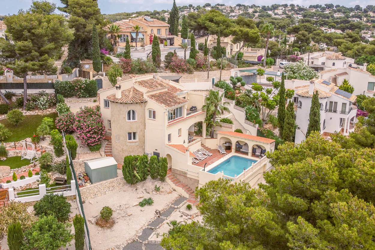 Luftaufnahme der nach Süden ausgerichteten Villa mit Natursteinturm, terrassiertem Garten und 8x4m Pool mit überdachtem Grillbereich und Sonnenterrasse.