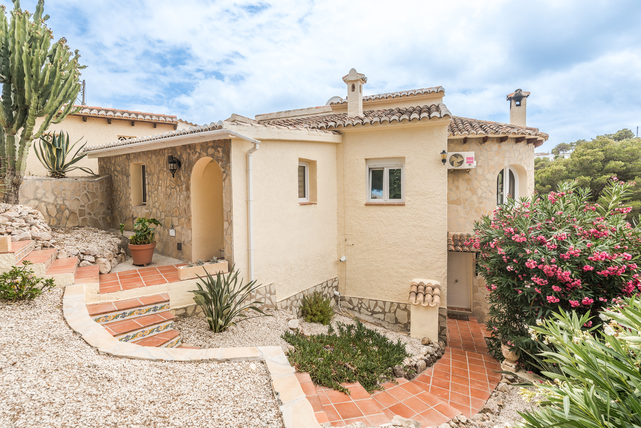 Mediterrane Außenansicht mit Natursteinwänden, Terrakottatreppen mit dekorativen Fliesen und einem pflegeleichten Garten mit Sukkulenten und Oleander.