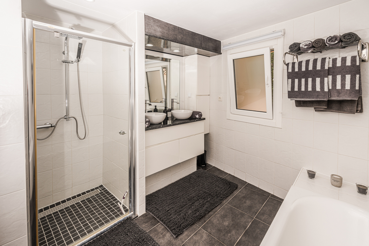 Modernes Badezimmer mit Glasduschkabine, Doppelwaschbecken auf dunkler Platte und kontrastierenden anthrazitfarbenen Bodenfliesen.